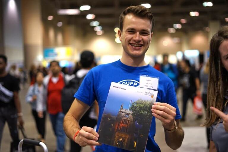 A McMaster student holding up a viewbook at the Ontario Universities fair