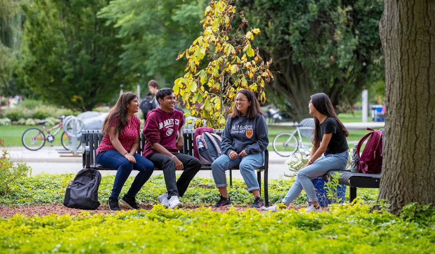 Four students sitting together on a bench on campus
