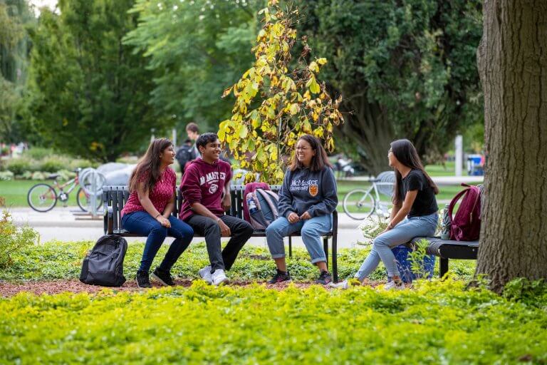 Four students sitting together on a bench on campus