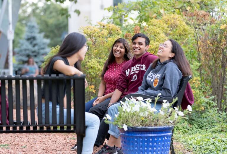 Four students laughing on a bench on campus