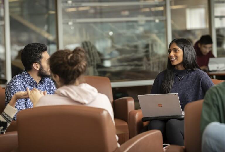 Three students sitting with their laptops and talking in the library