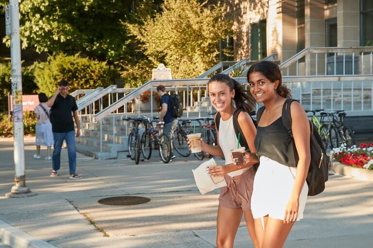 Two students walking outside the McMaster student centre with coffee in their hands