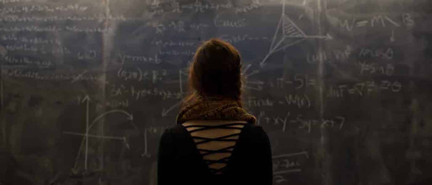 A backshot of a student looking at a chalkboard filled with equations