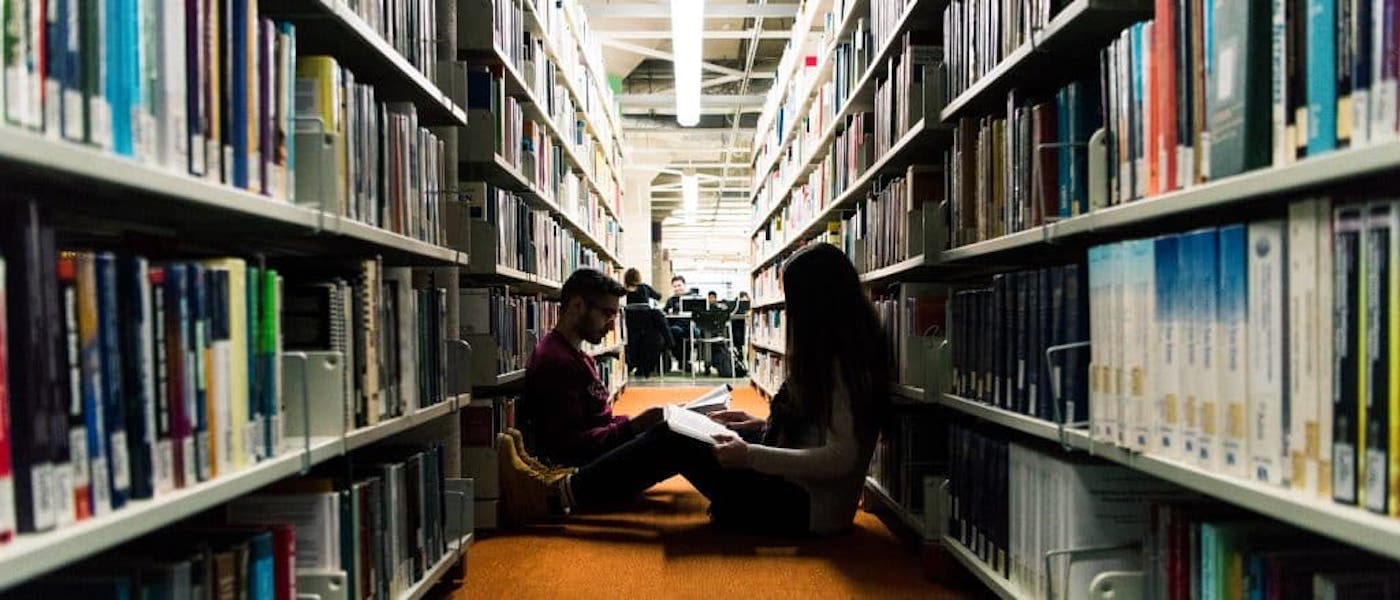 Two students studying on the floor of an aisle in a library