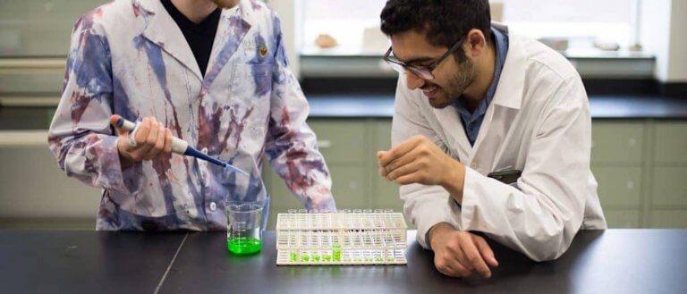 Two students in a lab working with vials and a beaker
