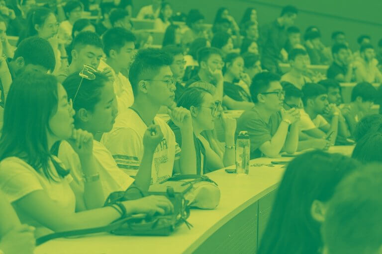 A green yellow duotone image of a large group of students in a lecture hall