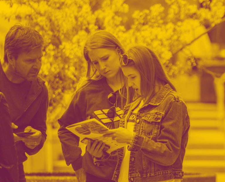 A maroon yellow duotone image of three visitors reading a campus map