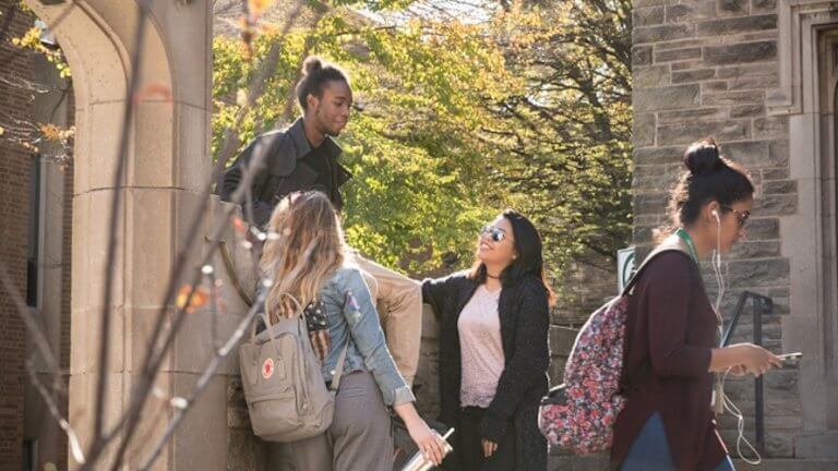 Three students standing beside the McMaster archway talking and laughing