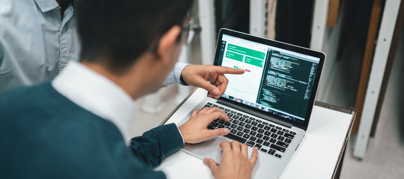 Two students working on a code together on a Macbook