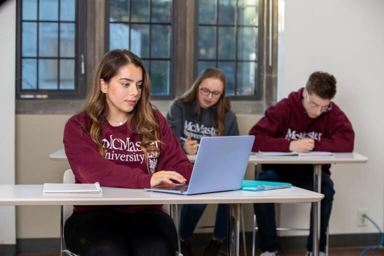 Three students wearing McMaster sweaters studying in a classroom
