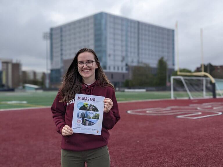 Student tour guide holding 2022 viewbook in McMaster football field