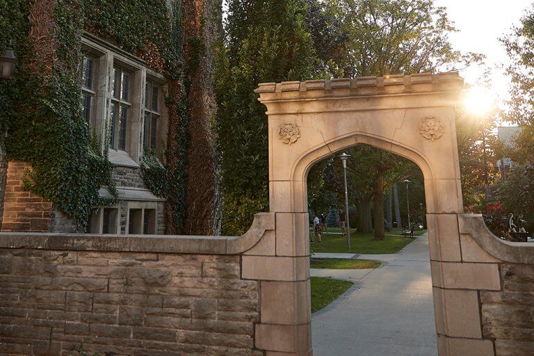 A portrait view photo of the sun setting over the Edwards Arch in McMaster University campus.